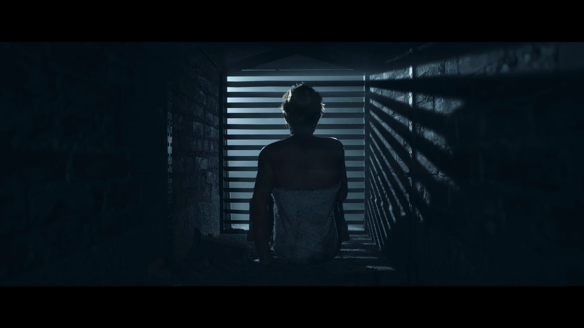 《Until Dawn™》游戏画面:一名身影站在狭窄昏暗的走廊中。